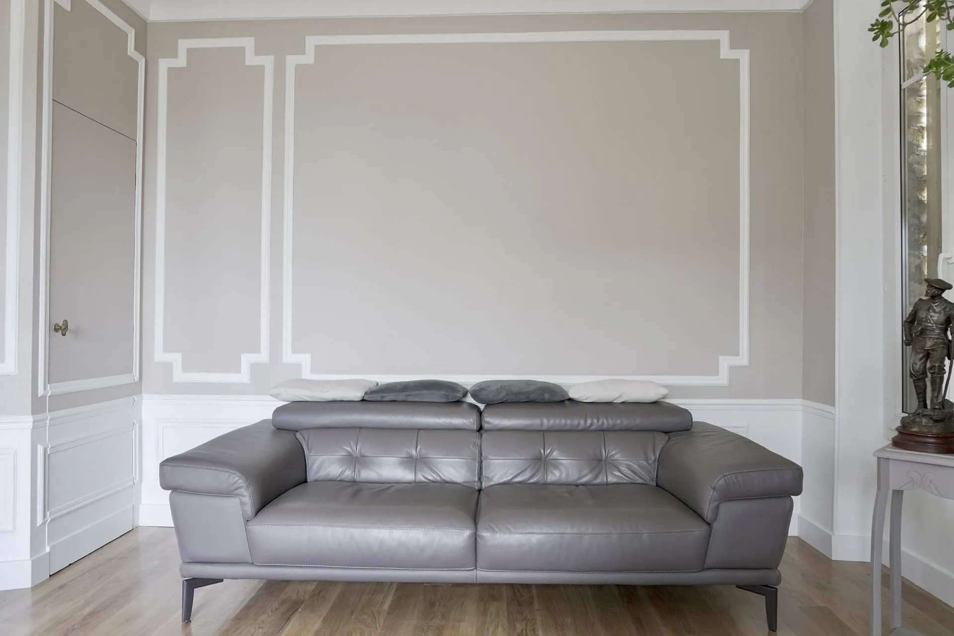 Salon rénové : murs peints à moulures, canapé gris et sol à l'aspect bois